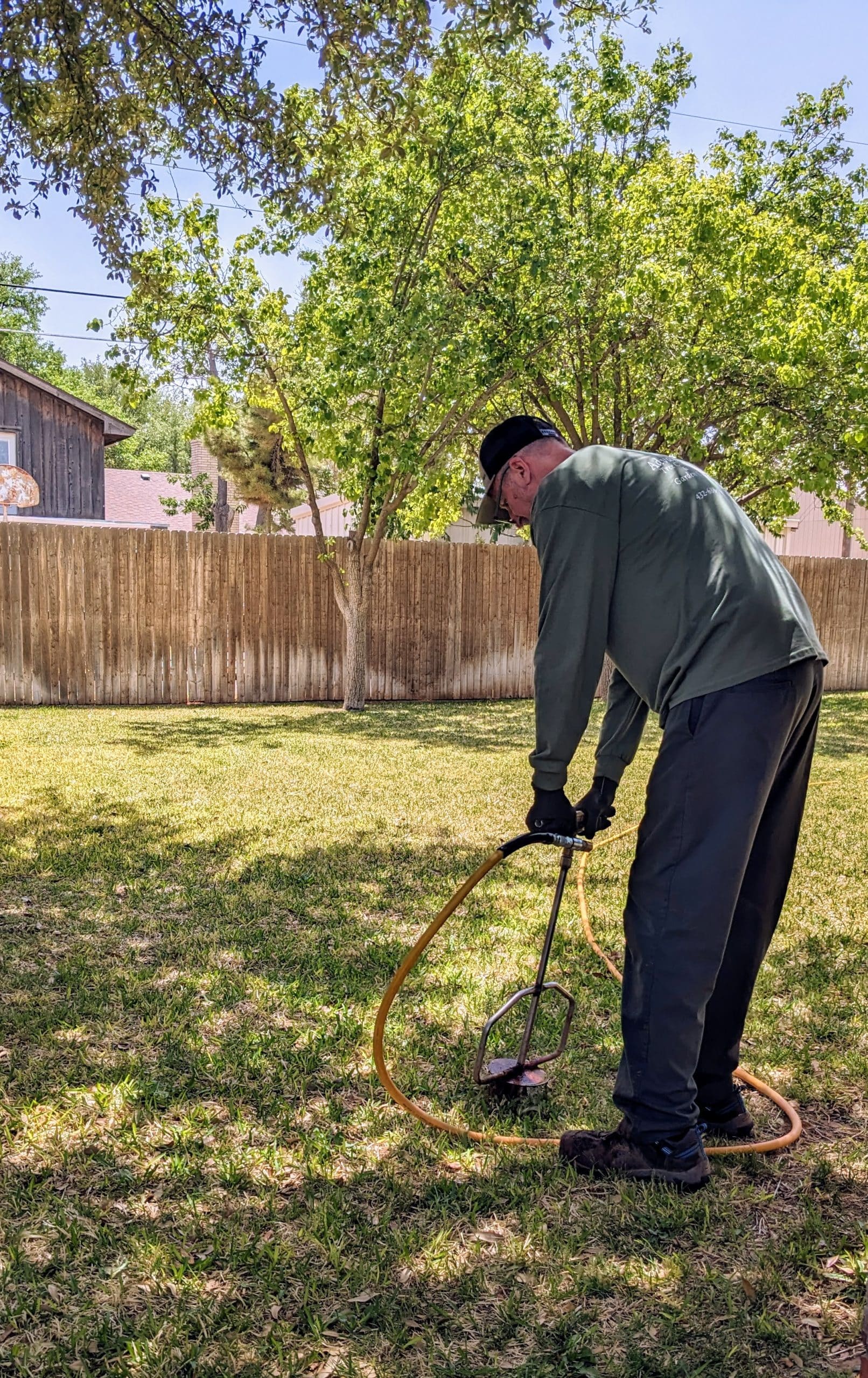 man in a backyard performing a root feeding service by sticking a device into the ground