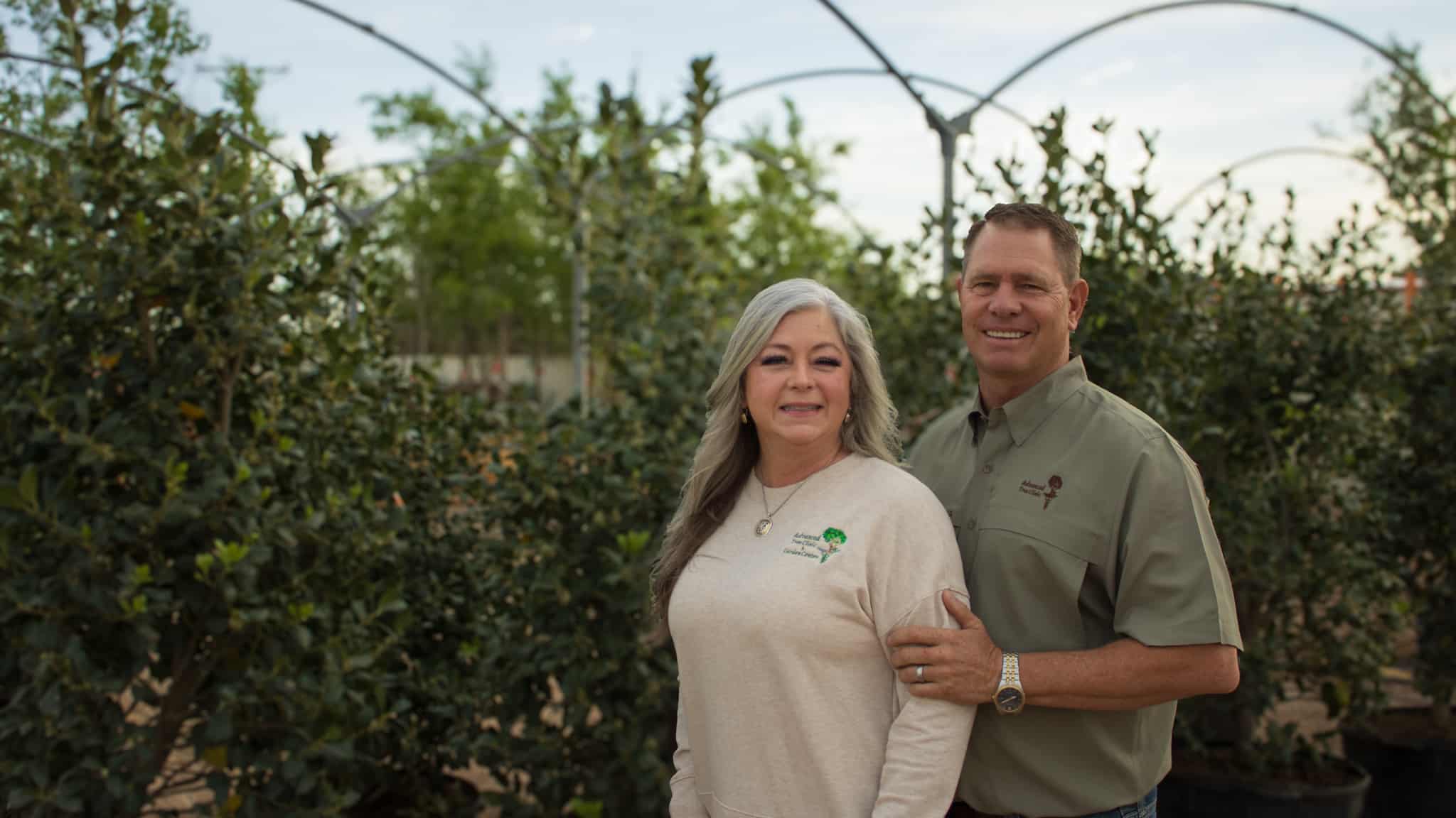 man and woman posing for picture in front of shrubs